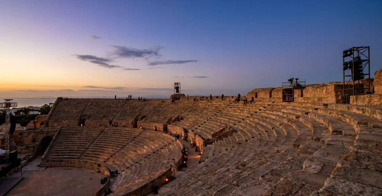 Vue panoramique du théâtre antique de Carthage illuminé au crépuscule avec des spectateurs arrivant progressivement