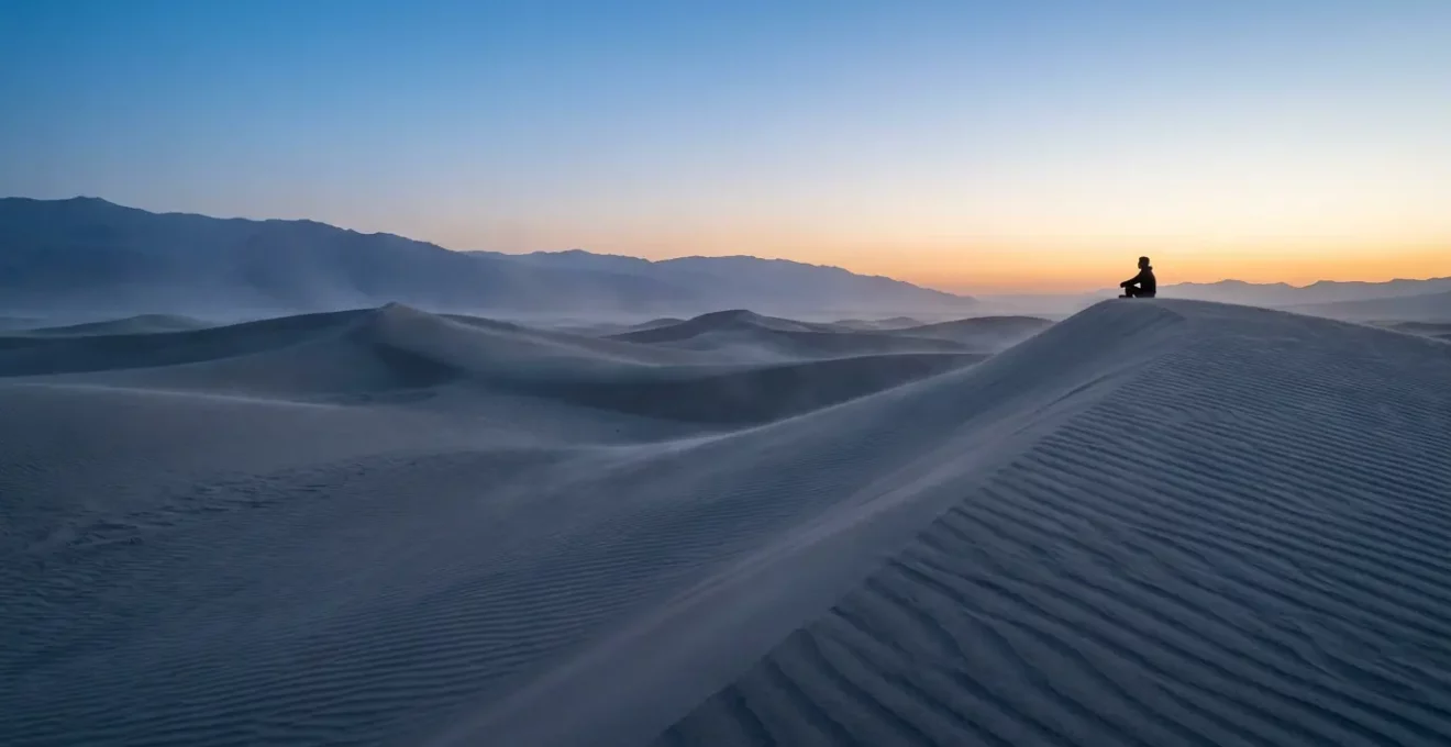 Voyageur assis en méditation face à l'immensité silencieuse du désert au crépuscule